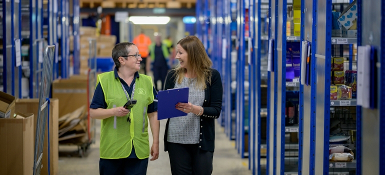 Two women in the warehouse are talking about warehouse management systems. 