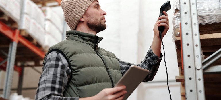 A man scanning products in a warehouse and thinking of warehouse management systems. 