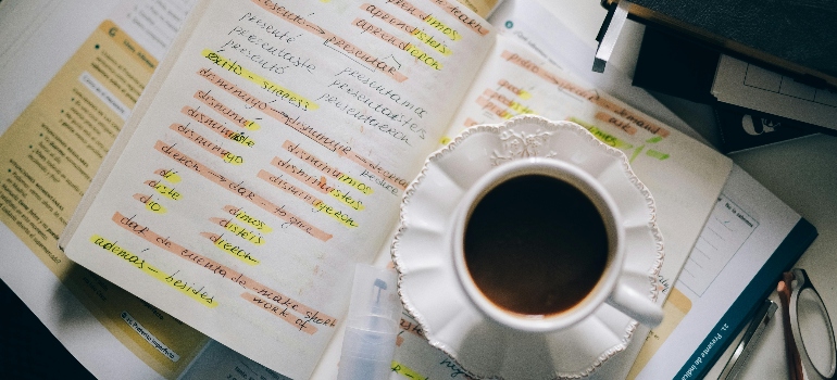 A Cup of Black Coffee on a Notebook with Notes of Foreign Language with Translation