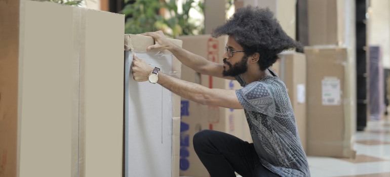 A man taping some boxes in the office after researching about how important communicating effectively with your team about the move is.