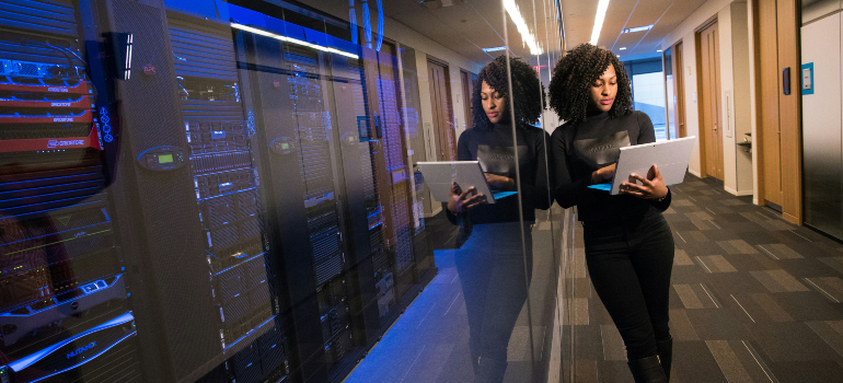 woman standing next to server racks and using a laptop