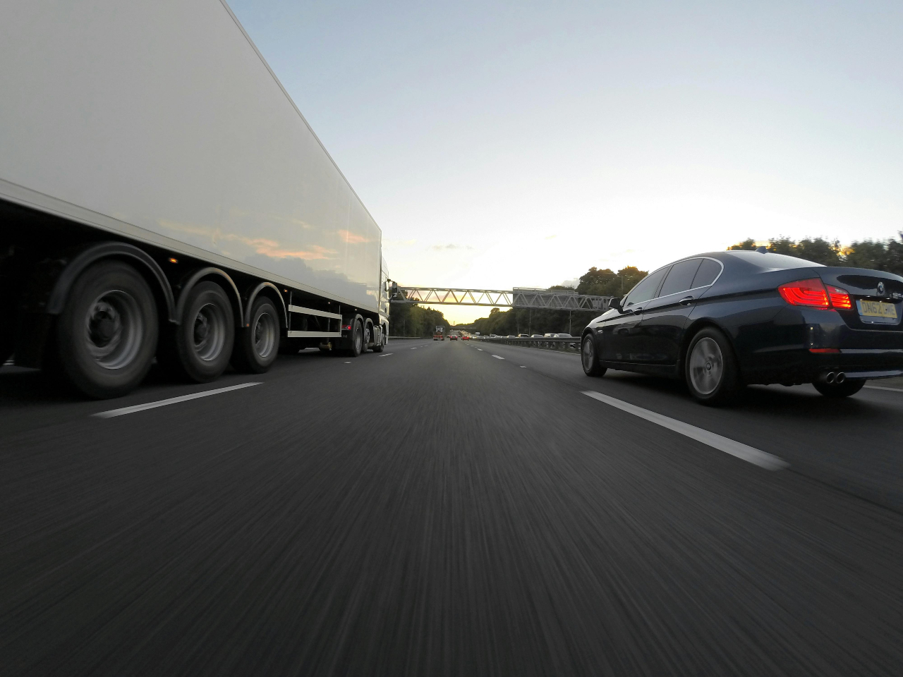 A car and a transport truck driving side by side on a highway.