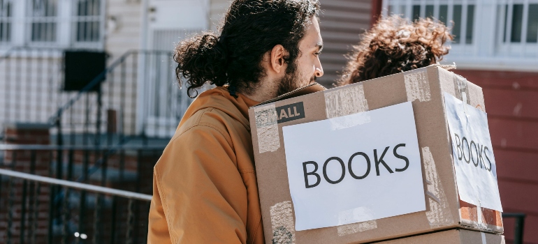 A man and a woman are carrying boxes on the street and discussing why fall is the perfect time to move in Washington, DC.