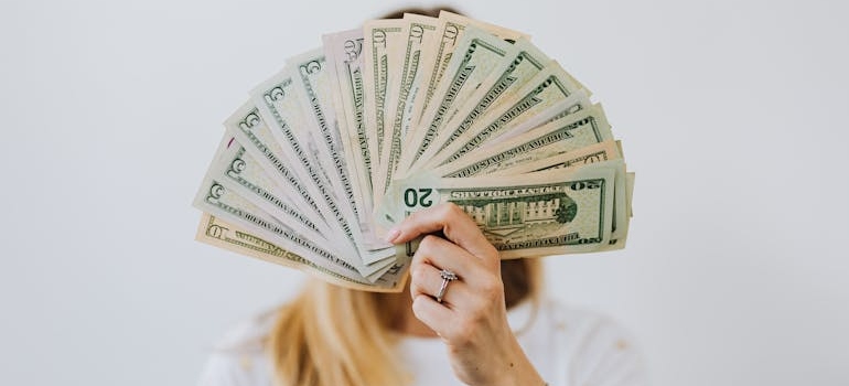 Woman Holding Fan of US Dollar Bills Wondering about The Hidden Costs of Choosing the Cheapest Rates