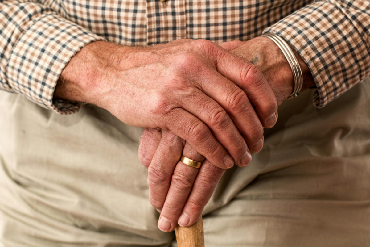 Close-up of an elderly man's hands resting on a cane.